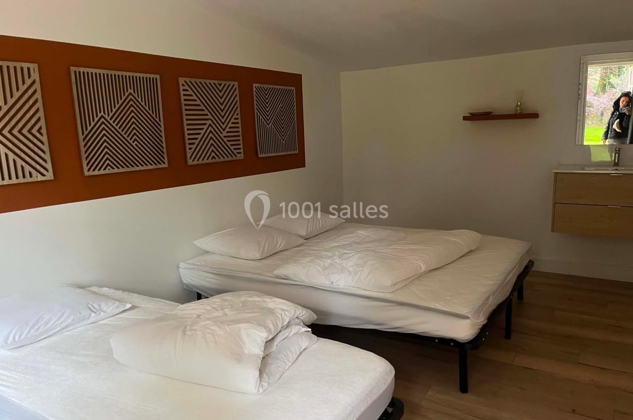Deux lits simples avec draps blancs dans une chambre lumineuse, décorée de cadres géométriques et d'un meuble minimaliste.