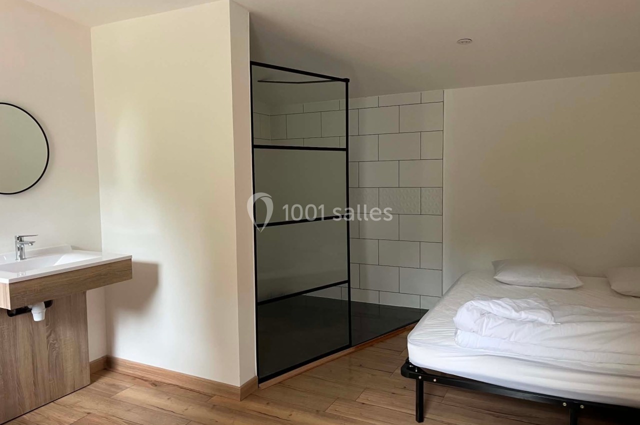 Chambre avec lit, lavabo mural et douche à l'italienne séparée par une paroi vitrée noire.