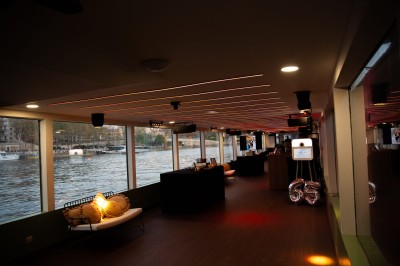 Miniature Location salle Paris 5 (Paris) - Péniche Amour #5 Terrasse d'un bateau aménagée avec des tables et des sièges, vue sur la tour Eiffel et un pont au coucher du soleil.