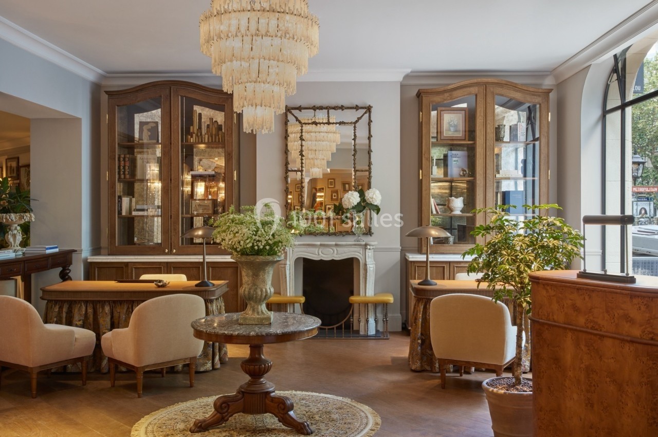 Salon élégant avec mobilier classique, lustres en cristal, cheminée ornée et grandes vitrines en bois.