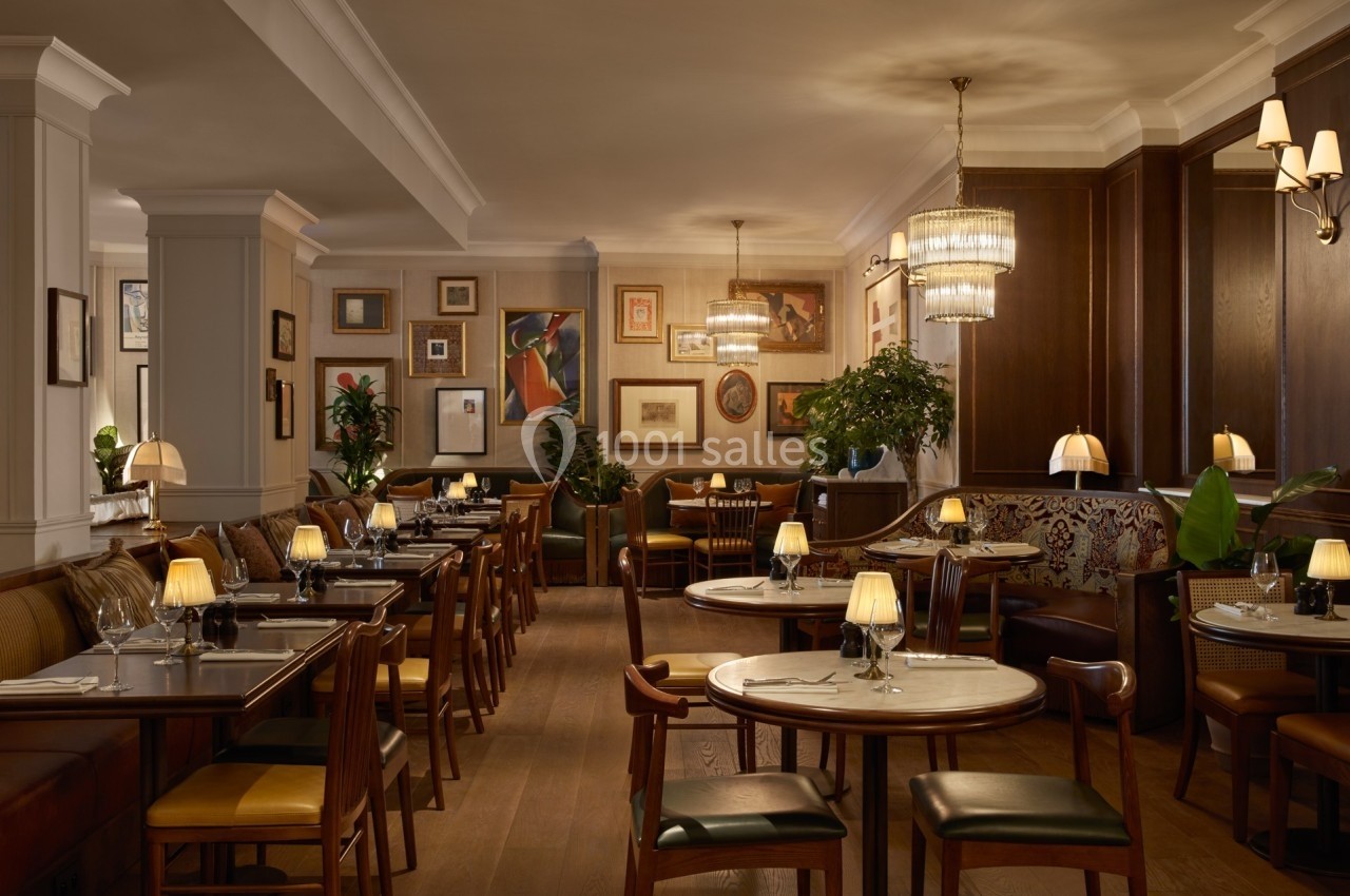 Salle de restaurant élégante avec tables en bois, chaises rembourrées, éclairage tamisé et décorations murales artistiques.