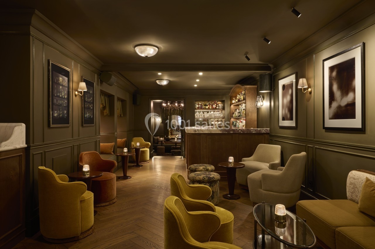 Salon élégant avec fauteuils colorés, tables basses, éclairage tamisé et bar en arrière-plan.