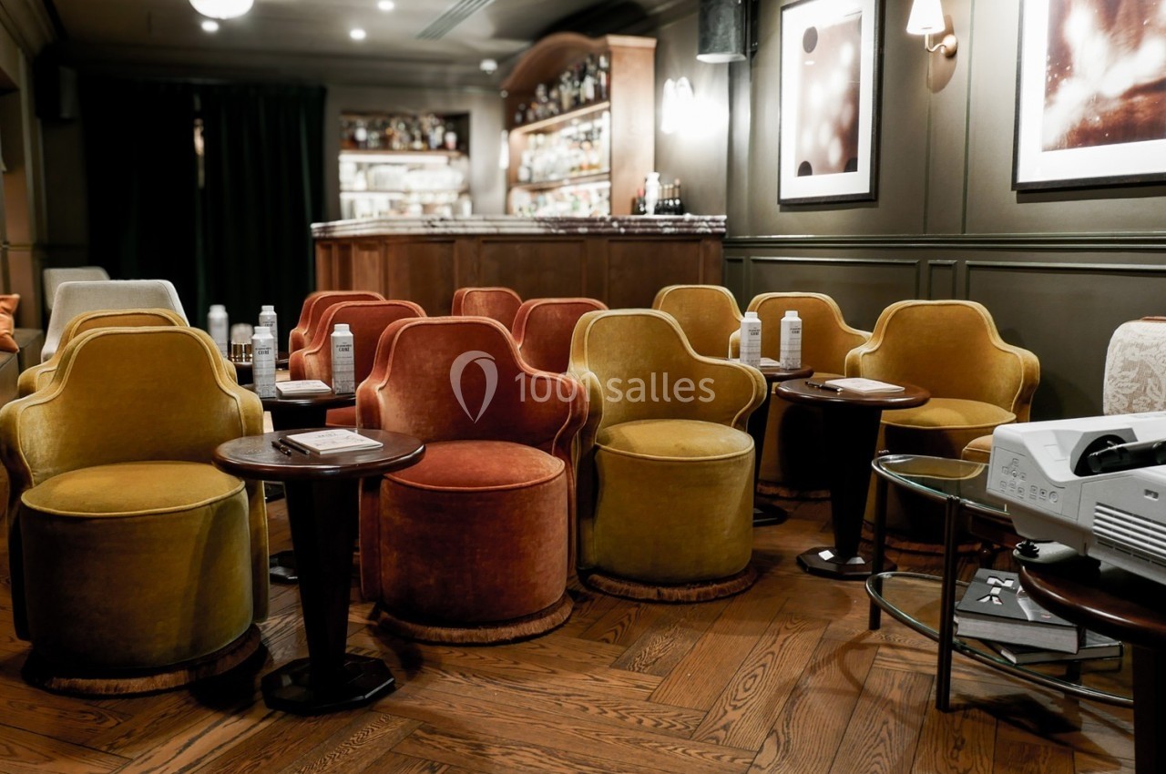 Salle de projection privée avec fauteuils colorés, tables basses, projecteur et bar en arrière-plan.
