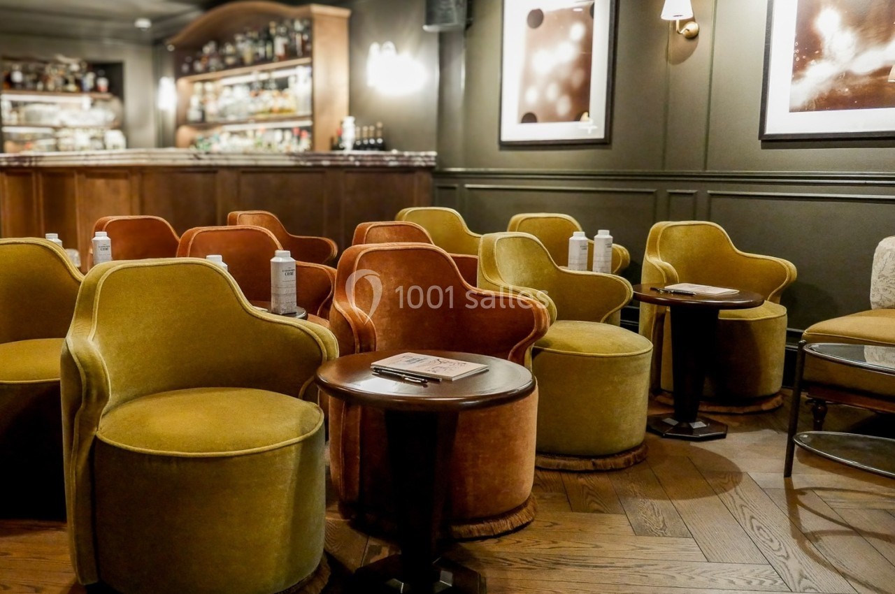 Fauteuils colorés disposés autour de petites tables dans un bar élégant avec un comptoir en bois en arrière-plan.