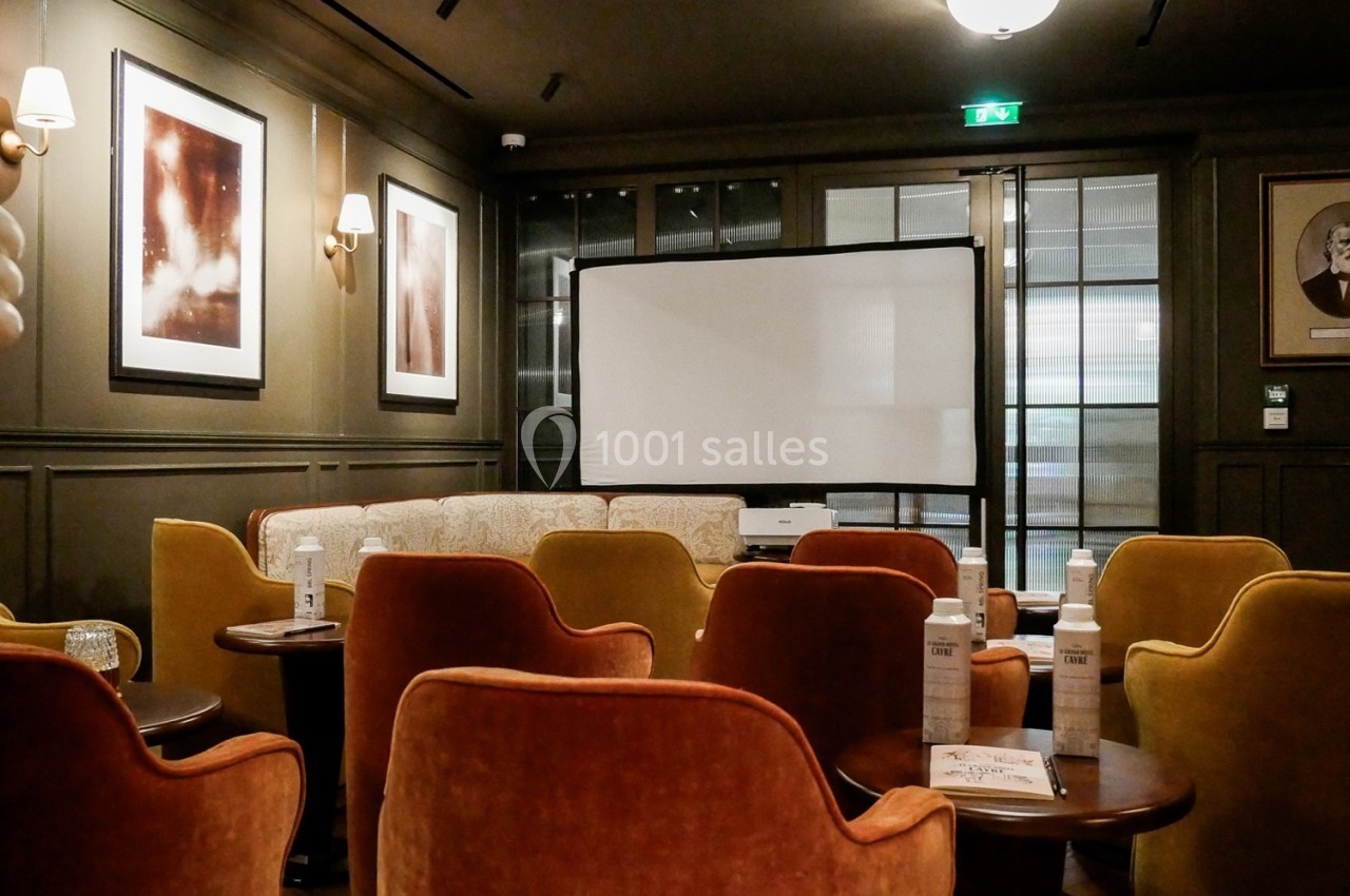 Salle de réunion avec fauteuils colorés, écran de projection, tables basses et décorations murales.