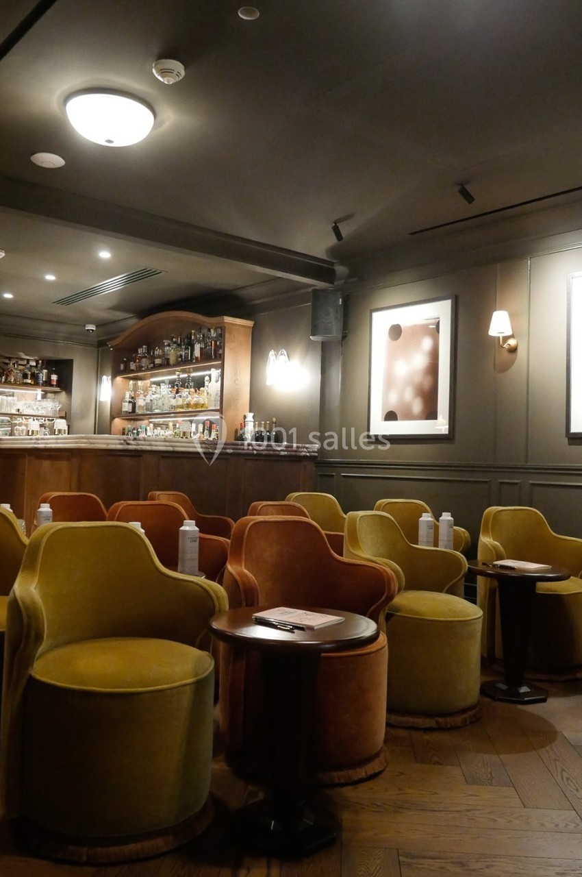 Salle de bar élégante avec fauteuils colorés, tables basses en bois et étagères de bouteilles en arrière-plan.