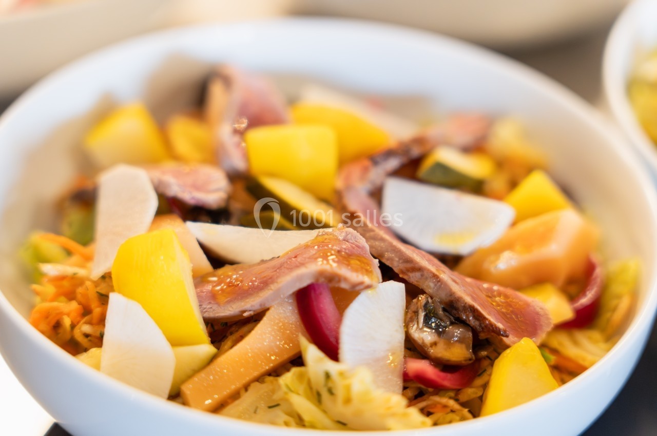 Bol de salade colorée avec légumes variés, tranches de poisson et morceaux de radis et mangue.