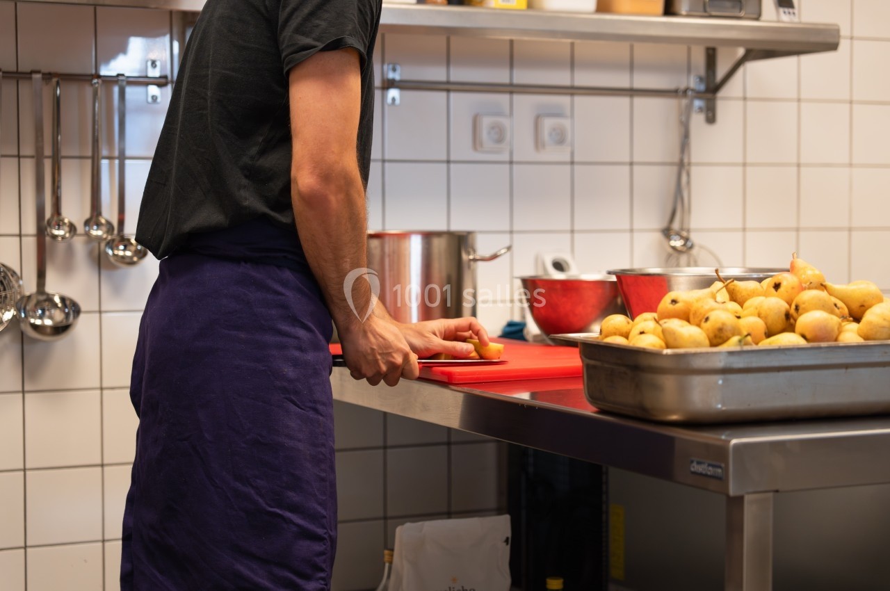 Un cuisinier découpe un ingrédient sur une planche rouge dans une cuisine professionnelle avec des poires à proximité.