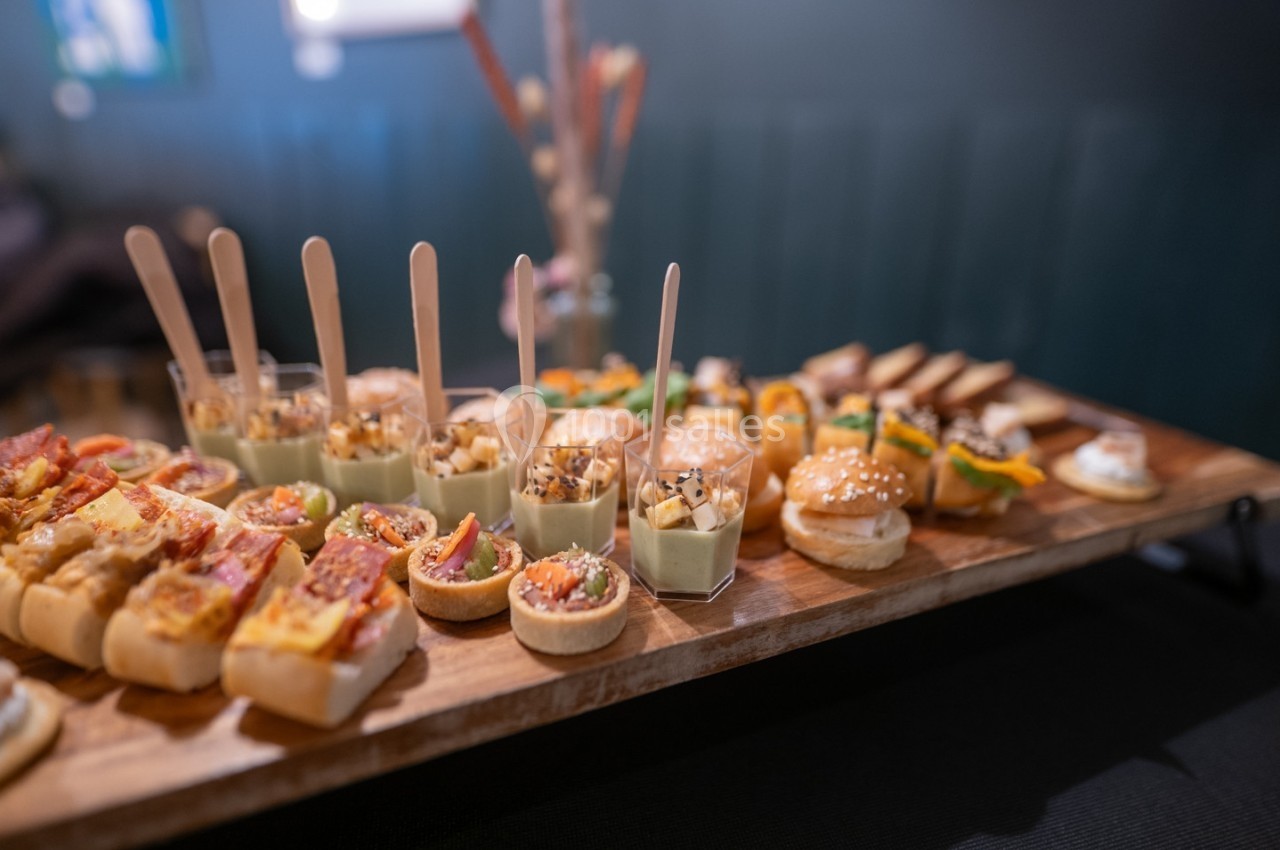 Plateau de bouchées apéritives variées, comprenant mini-burgers, verrines et tartes salées, disposé sur une table en bois.
