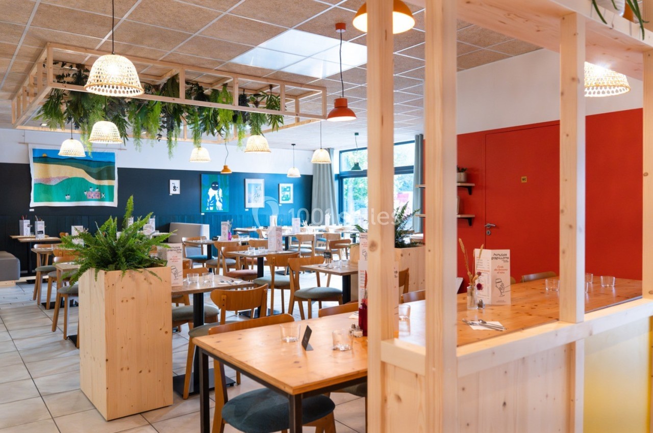 Salle de restaurant lumineuse avec tables en bois, plantes suspendues et décoration moderne.