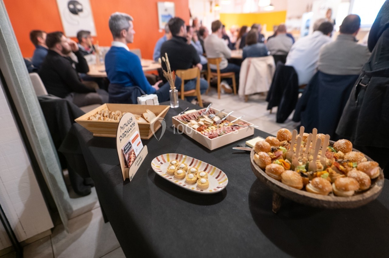 Buffet avec amuse-bouches variés sur une table noire, en arrière-plan des personnes assises lors d'une réunion.