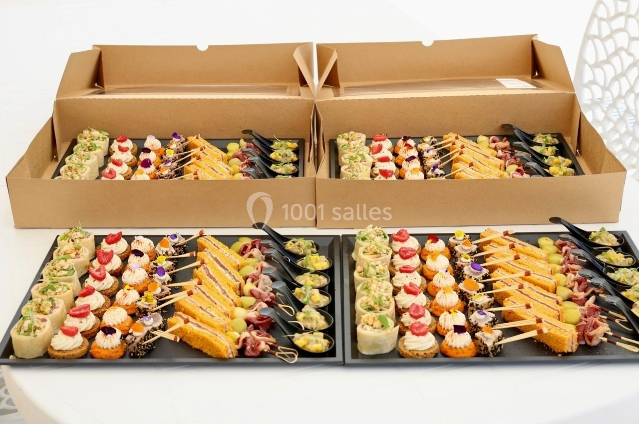 Plateaux de bouchées apéritives variées présentées sur des assiettes noires, avec des cartons d'emballage en arrière-plan.