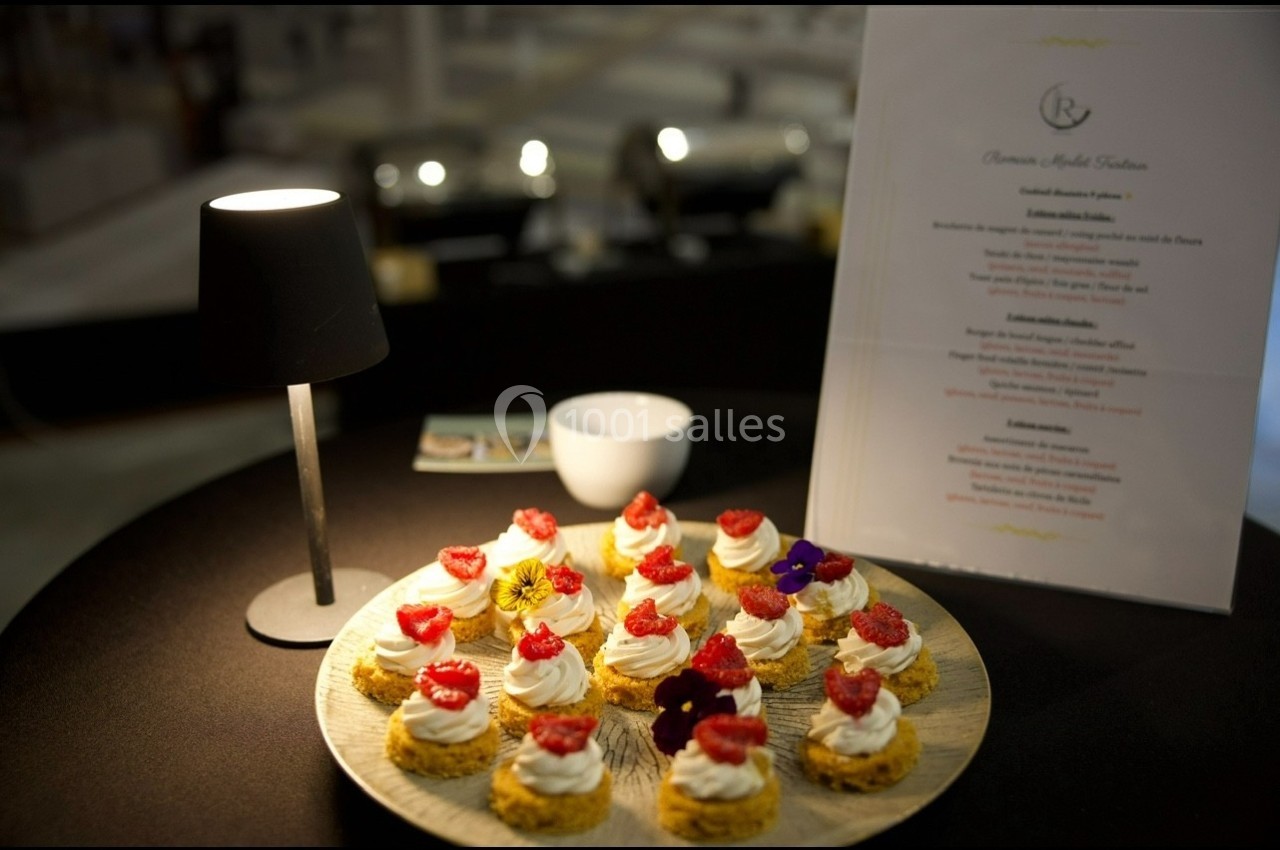 Assortiment de petits desserts garnis de crème et de framboises, présenté sur une table avec une lampe et un menu.