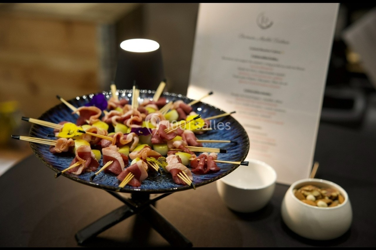 Plateau de brochettes apéritives colorées avec fleurs comestibles, accompagné de bols et d'un menu en arrière-plan.