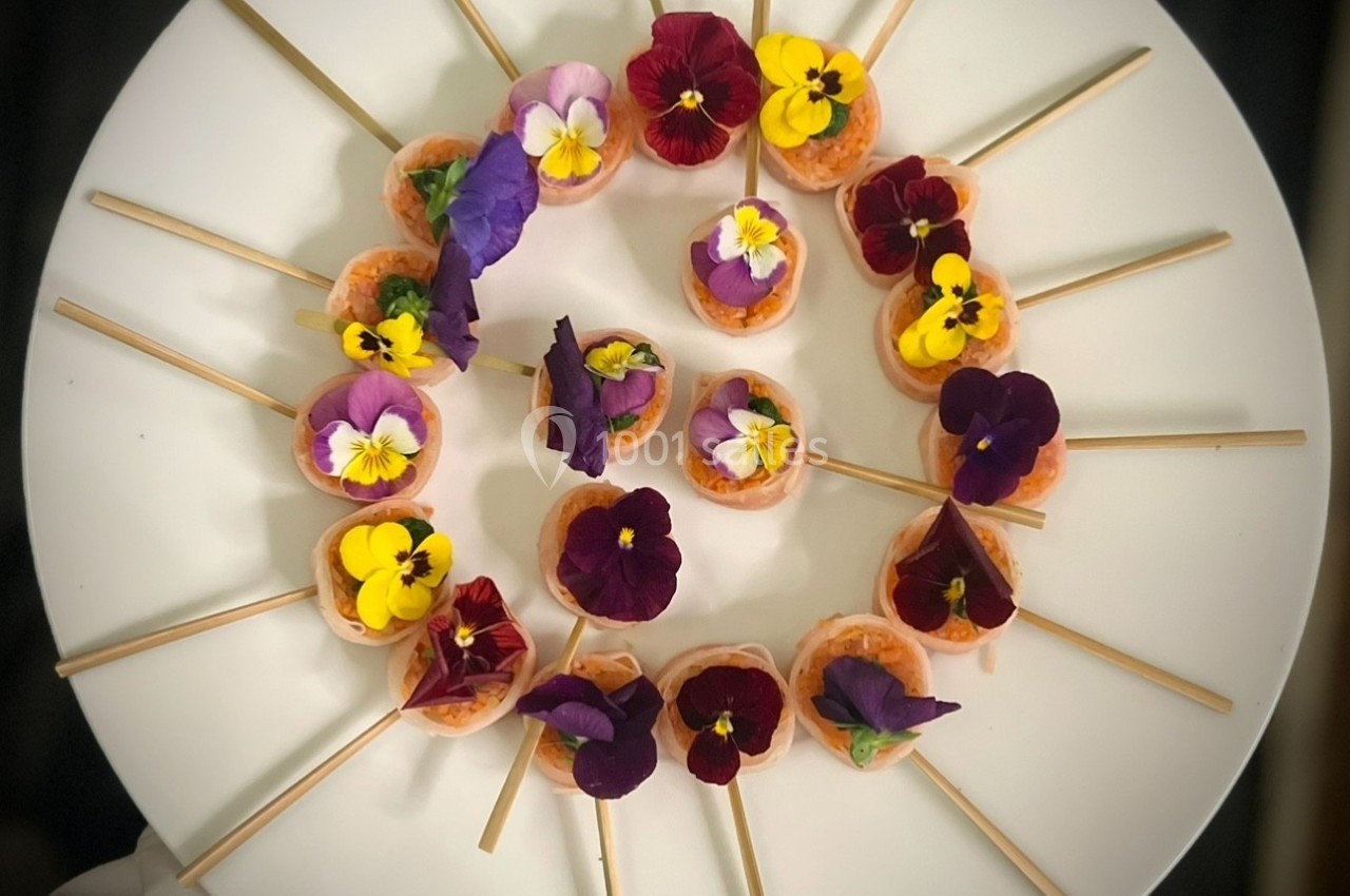 Assortiment de bouchées sur des piques, décorées de fleurs comestibles colorées, disposées en cercle sur une assiette…