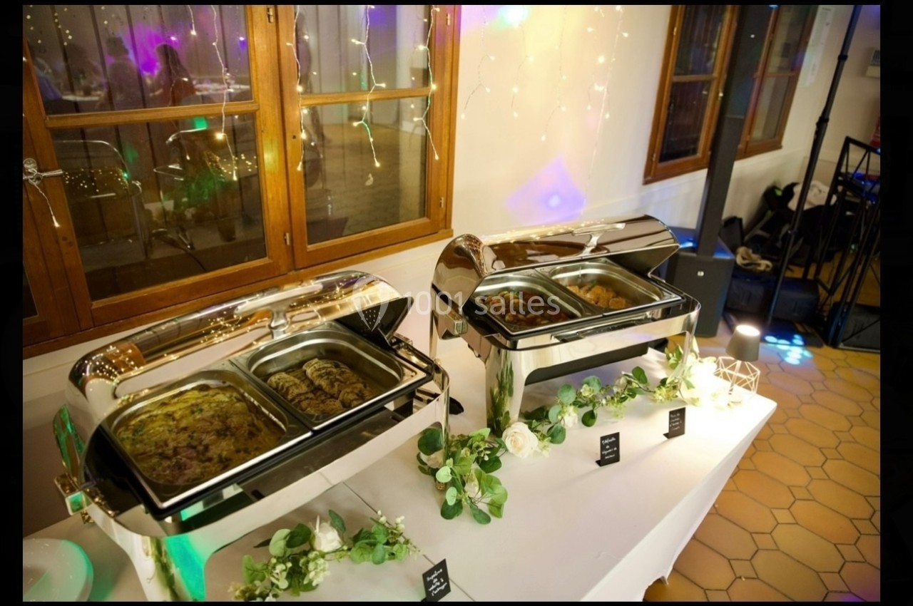 Buffet chaud avec plats variés présentés dans des chafing dishes en inox, décoré de guirlandes et de fleurs.