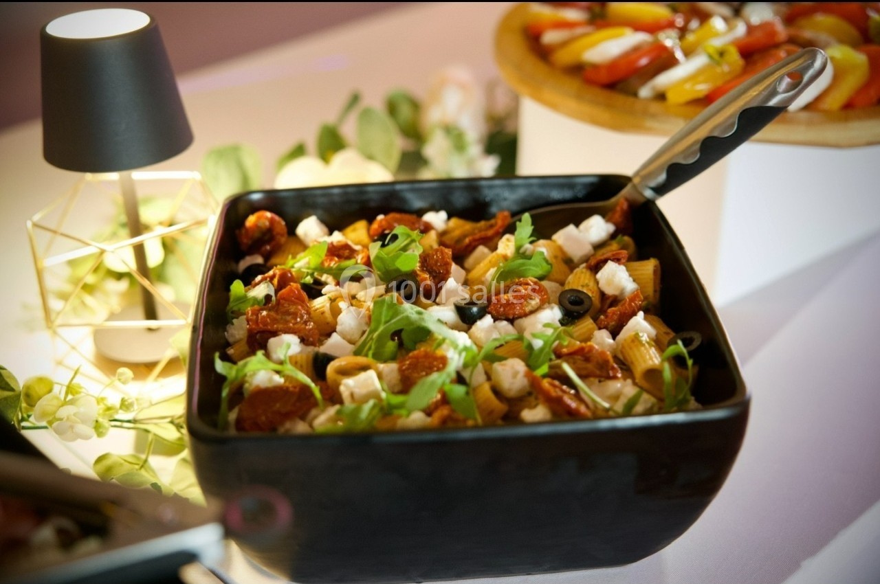 Salade méditerranéenne dans un bol noir, garnie de roquette, tomates séchées, olives noires et fromage, sur une table…