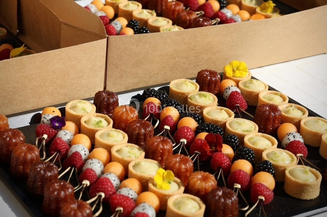 Plateau de mini-pâtisseries variées, incluant cannelés, tartelettes et fruits frais, disposées sur des brochettes.
