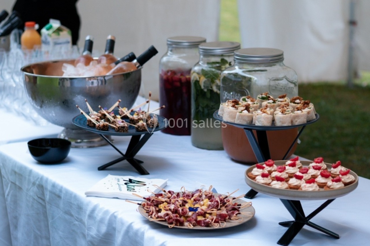 Buffet avec verrines, amuse-bouches, boissons en carafes et seau à glace sur une nappe blanche.