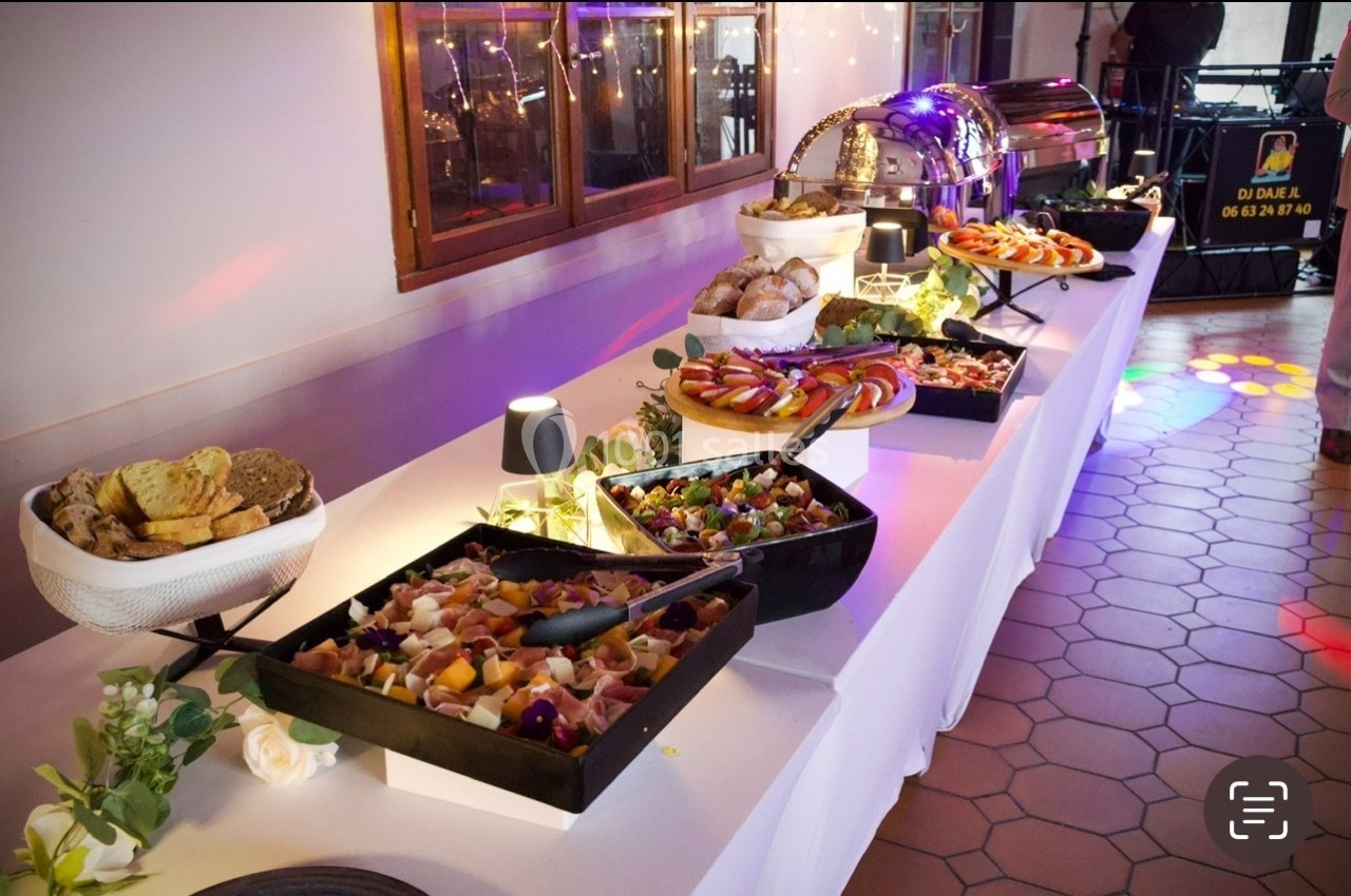 Buffet de réception avec plats variés, salades, pains et charcuteries disposés sur une table blanche éclairée.