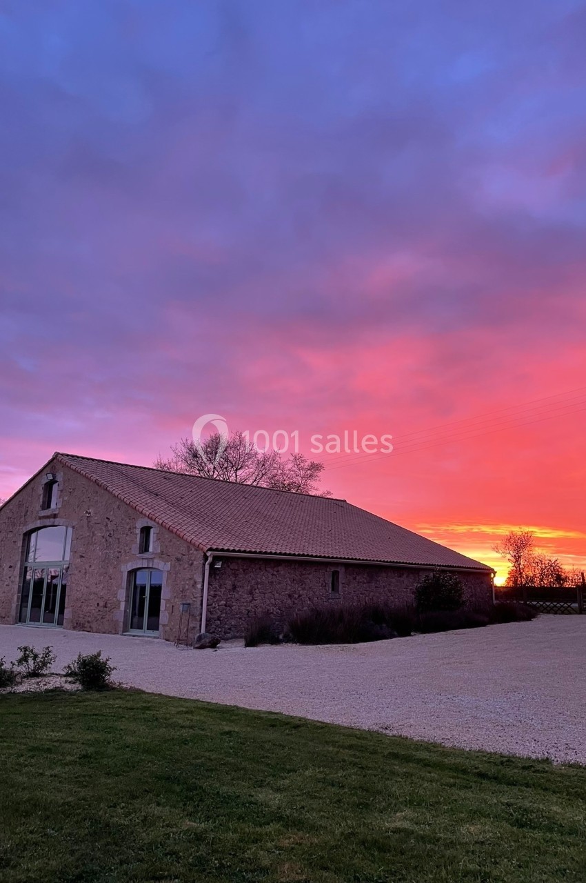 Bâtiment en pierre avec toit en tuiles, éclairé par un ciel de coucher de soleil aux teintes roses et violettes.