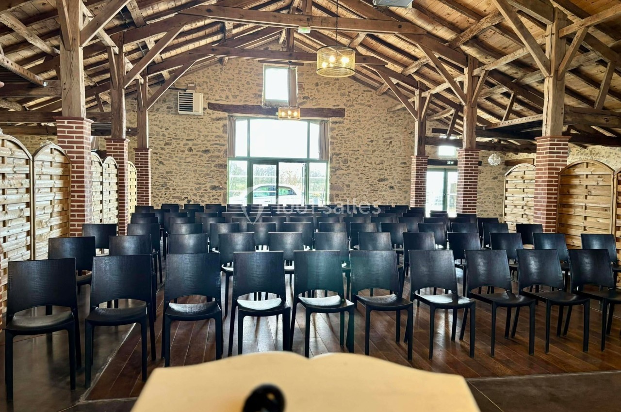 Salle de conférence en bois avec des rangées de chaises noires vides, vue depuis un pupitre au premier plan.