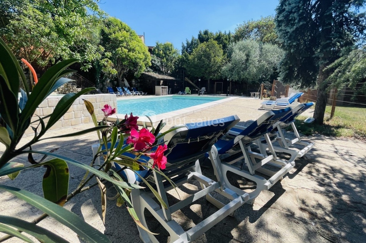 Chaises longues alignées près d'une piscine extérieure entourée de végétation et de fleurs sous un ciel dégagé.