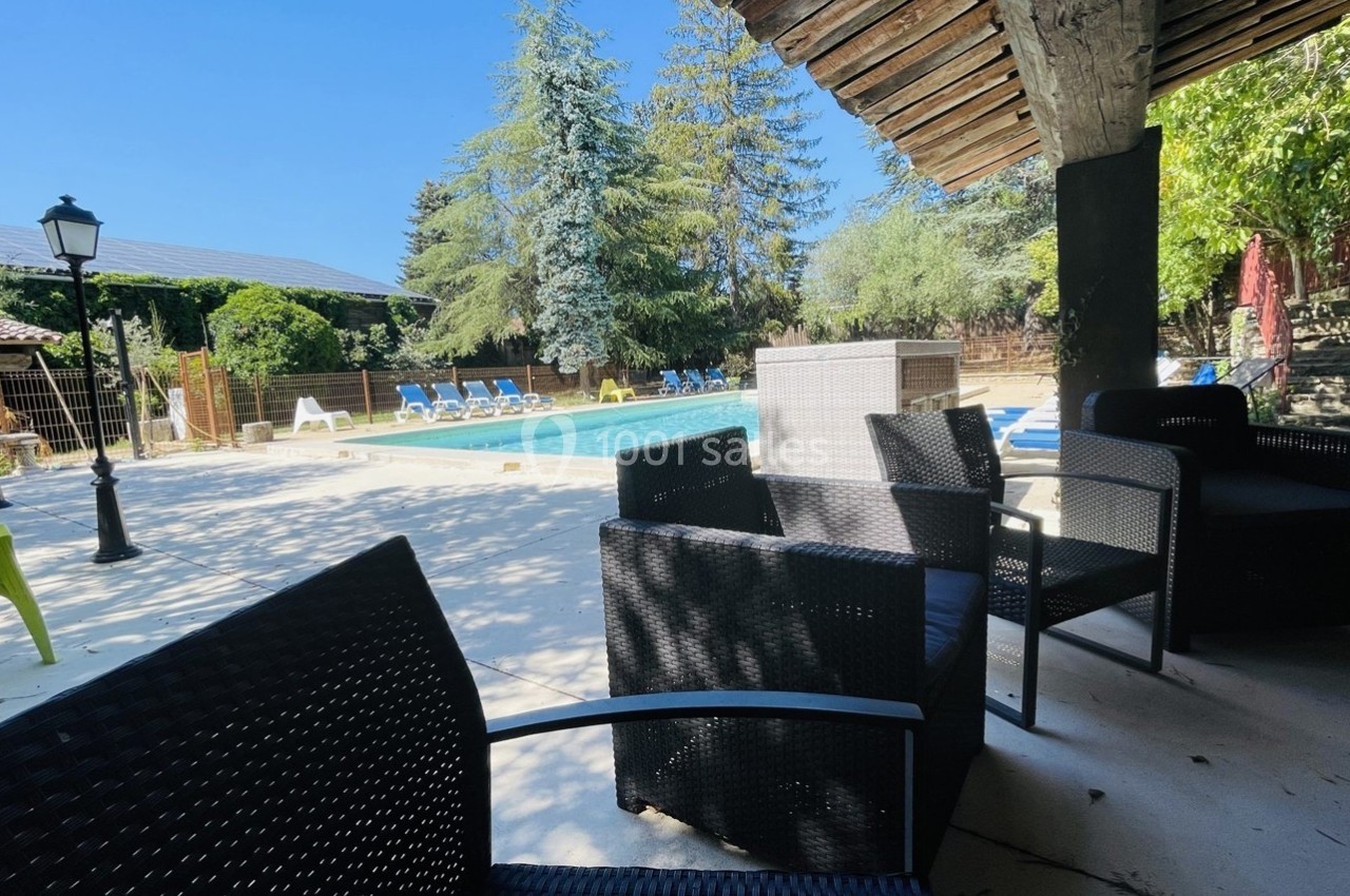 Terrasse ombragée avec fauteuils en rotin, vue sur une piscine entourée de transats et de végétation.