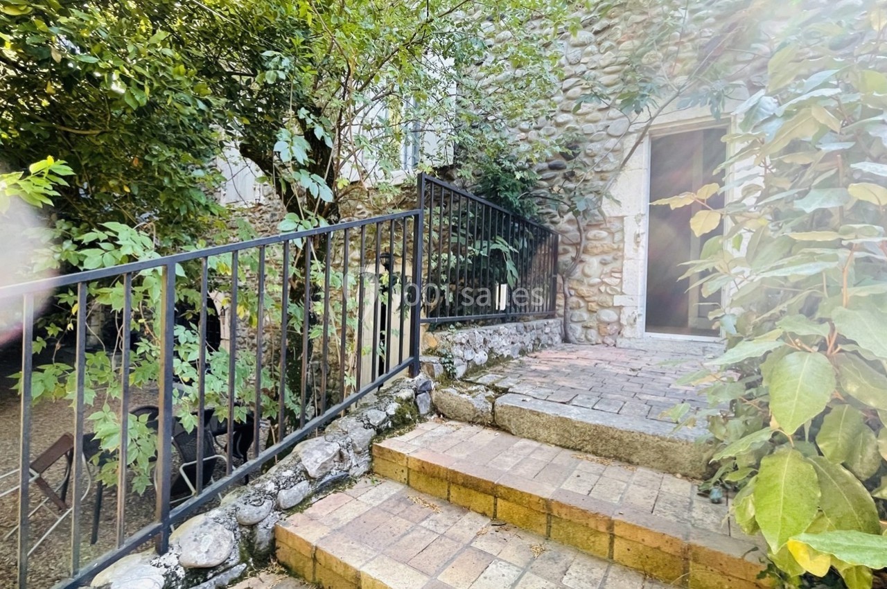 Escalier en pierre bordé de végétation menant à une porte encadrée de murs en pierre.