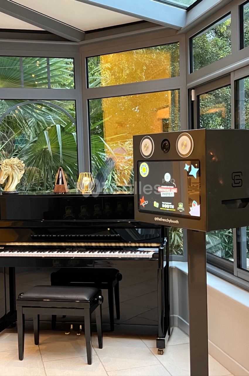 Piano noir devant une baie vitrée, accompagné d'une borne photo équipée d'un écran et de haut-parleurs.