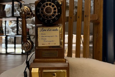 Téléphone rétro doré à cadran rotatif posé sur une surface blanche, avec un décor en bois et pierre en arrière-plan.