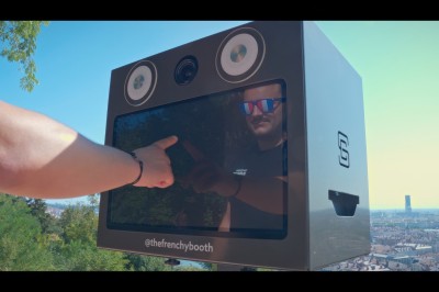 Une borne photo en bois avec écran et accessoires, entourée de personnes discutant dans un espace industriel.