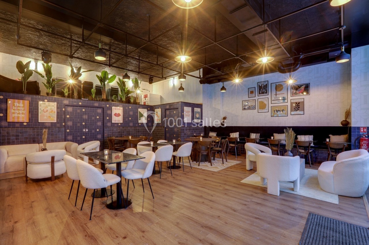 Salle de restaurant moderne avec mobilier clair, murs décorés de cadres et plantes disposées en hauteur.