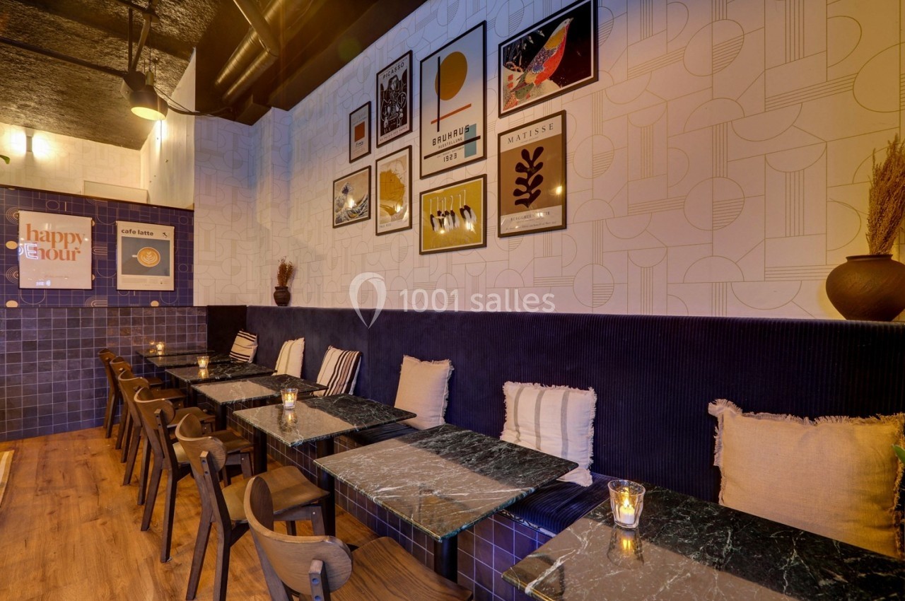 Salle de restaurant moderne avec tables en marbre, chaises en bois, coussins et décorations murales artistiques.
