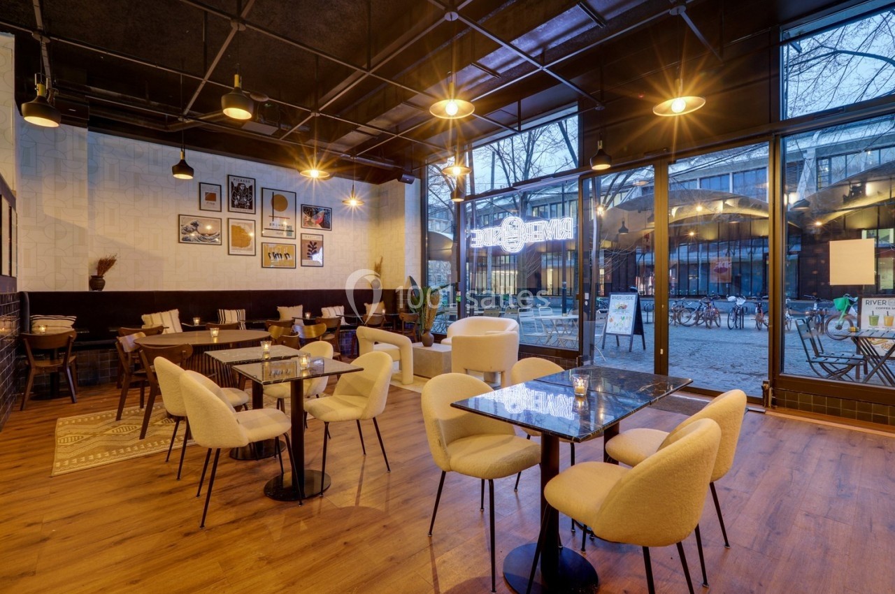 Salle de restaurant moderne avec tables en marbre, chaises beige et grandes baies vitrées donnant sur l'extérieur.