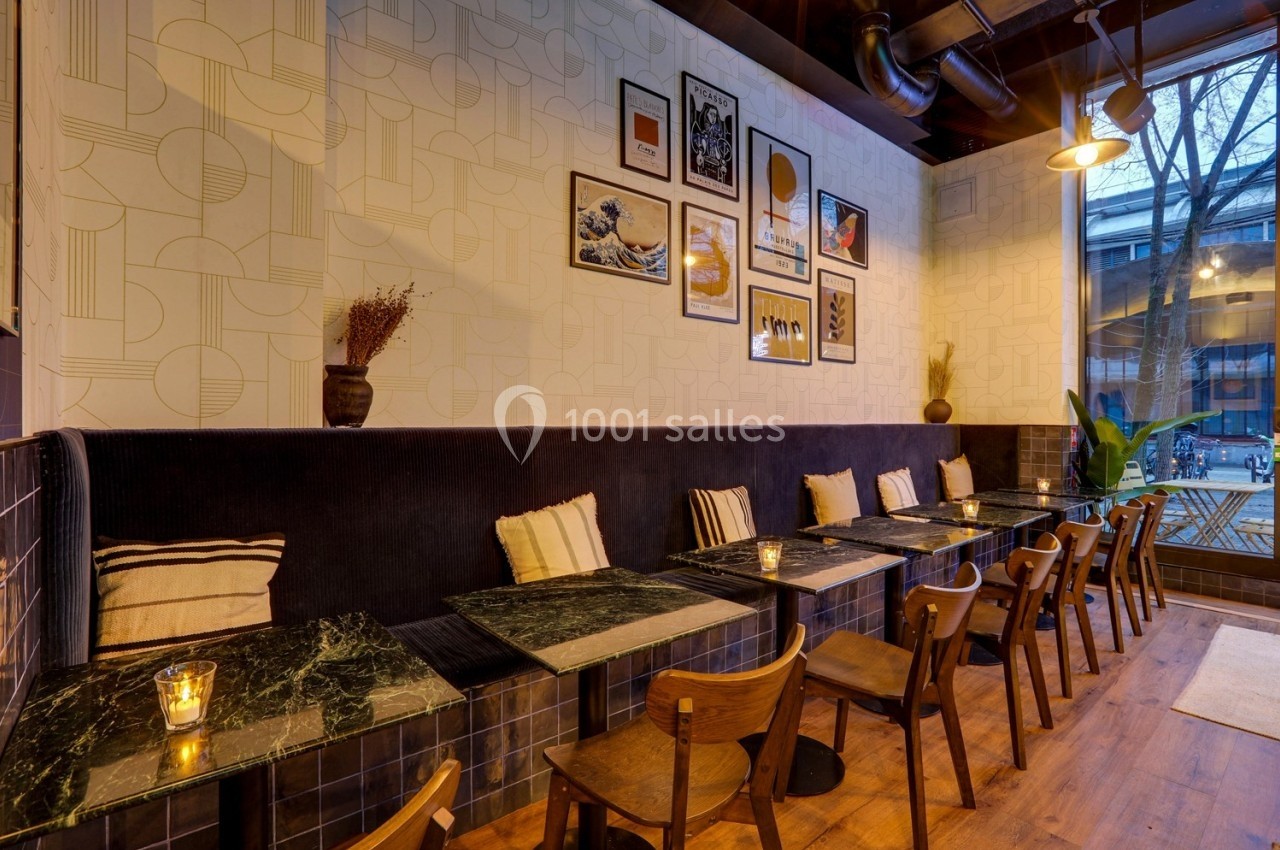 Salle de café avec tables en marbre, chaises en bois, banquette noire, décorations murales et lumière tamisée.