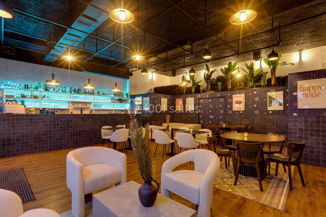 Intérieur d'un bar moderne avec des tables, des chaises, un éclairage chaleureux et un mur de bouteilles illuminé.