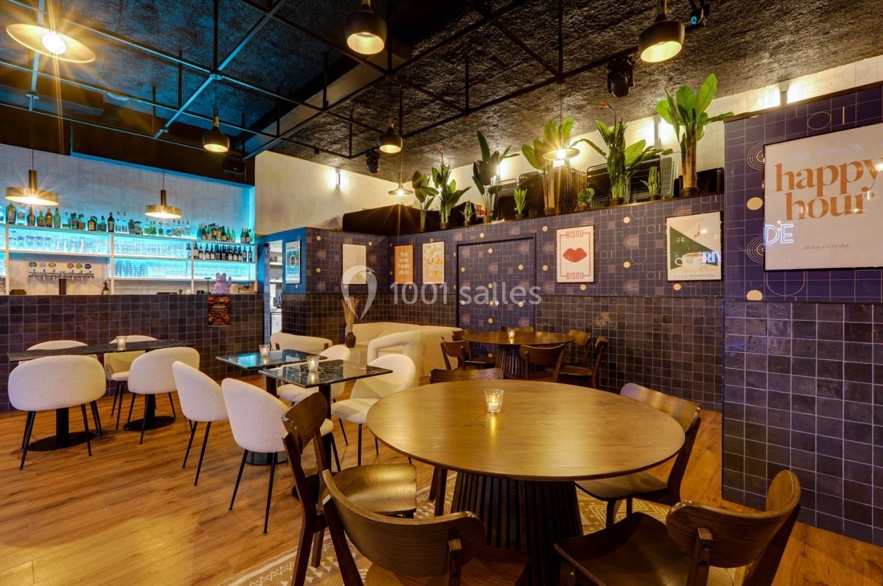 Intérieur d'un café moderne avec tables en bois, chaises design, plantes et éclairage chaleureux.