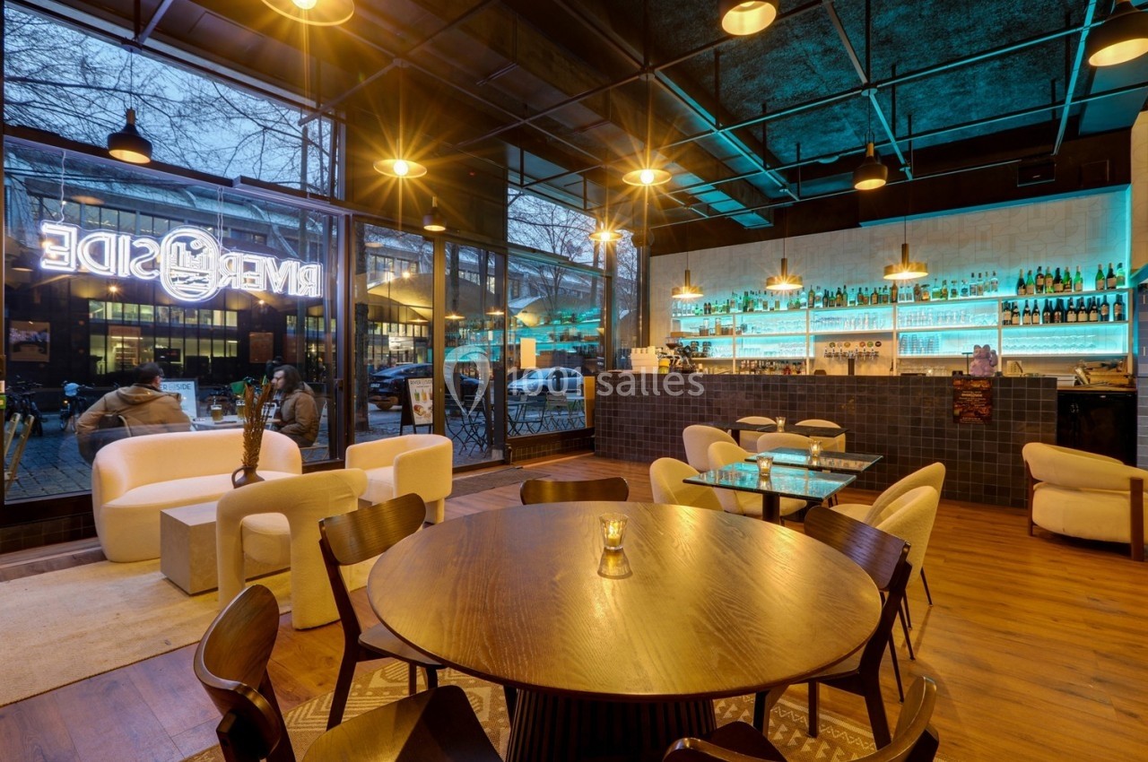 Intérieur d'un café moderne avec éclairage chaleureux, mobilier design et bar illuminé en arrière-plan.