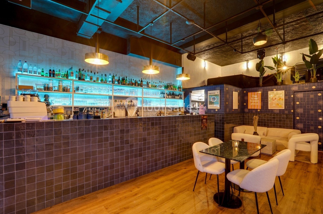 Intérieur d'un bar moderne avec comptoir éclairé, étagères de bouteilles, tables et chaises dans une ambiance chaleureuse.