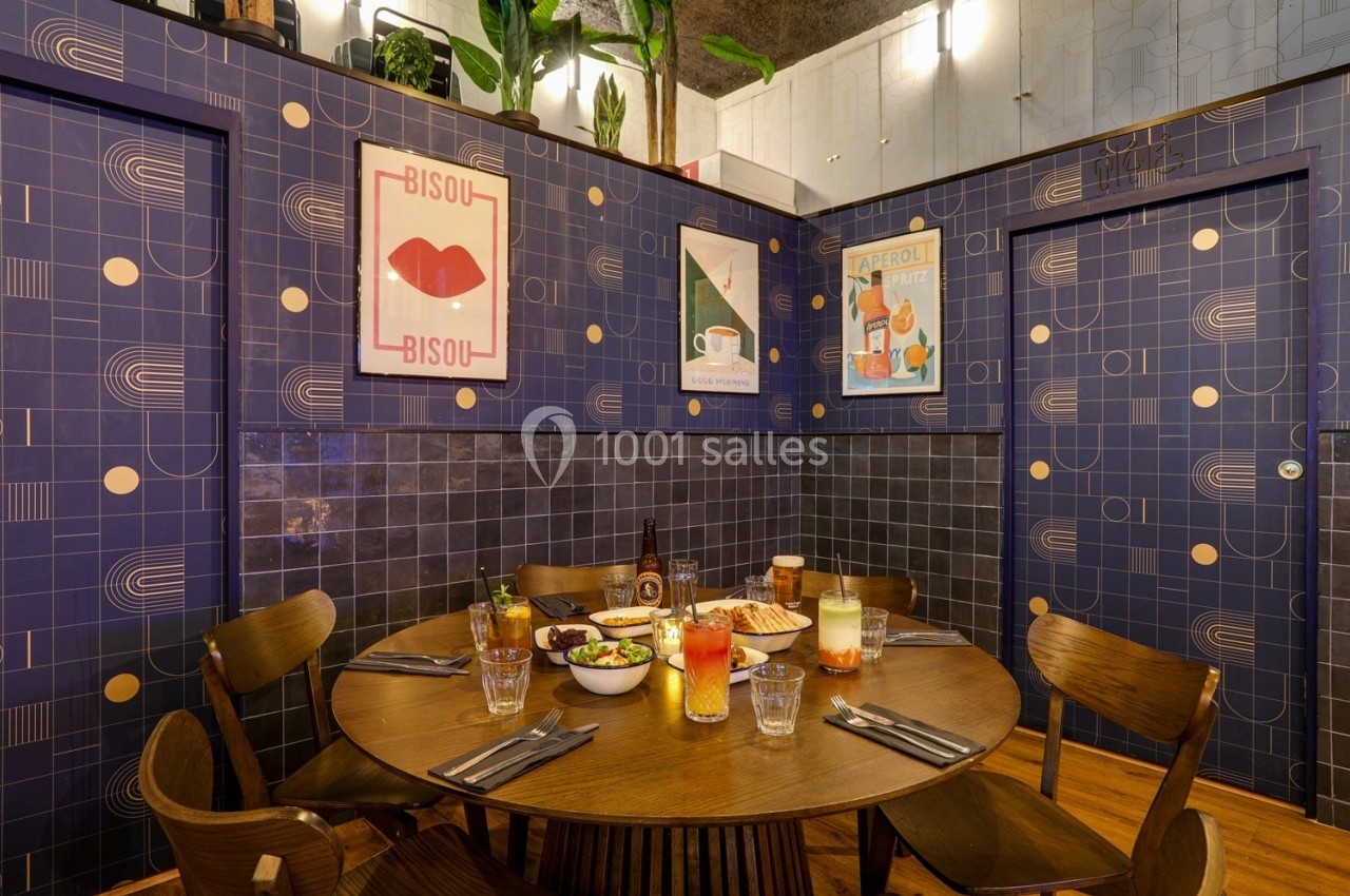 Table ronde dressée avec des plats et boissons, entourée de chaises en bois, dans une salle aux murs décorés de motifs…
