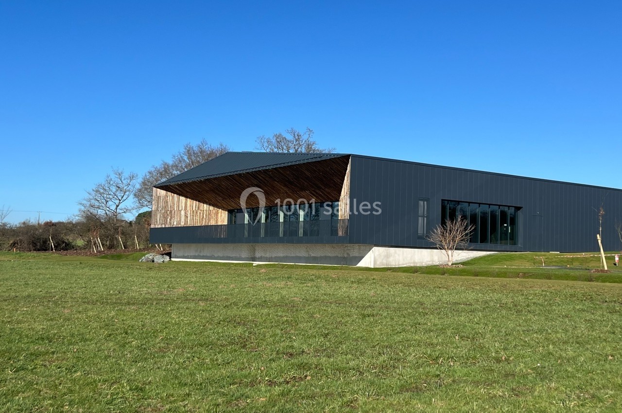 Bâtiment moderne avec façade en bois et métal, entouré d'une pelouse et d'arbres sous un ciel bleu.
