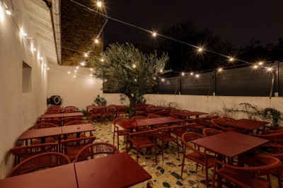 Bar avec comptoir en carrelage sombre, tabourets en bois, étagères avec bouteilles et verres, éclairage suspendu.