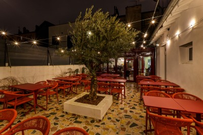 Bar avec comptoir en carrelage sombre, tabourets en bois, étagères avec bouteilles et verres, éclairage suspendu.