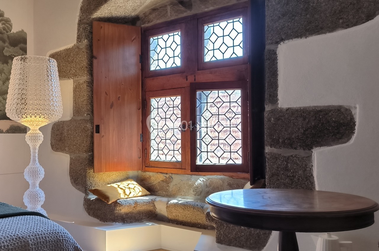 Fenêtre ancienne avec vitraux, encadrée de pierre, un banc intégré et une lampe moderne à côté.