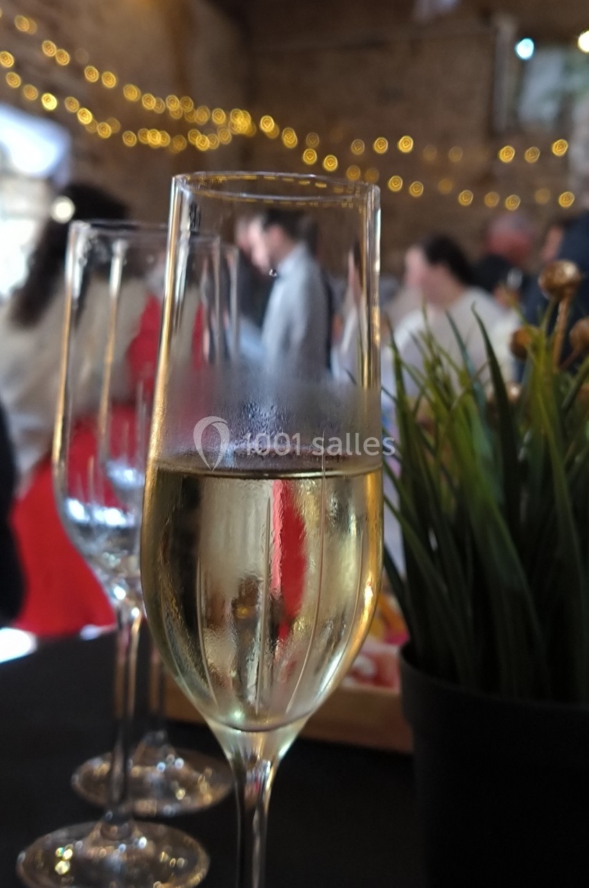 Verre de champagne sur une table, avec des invités flous en arrière-plan et des lumières décoratives.