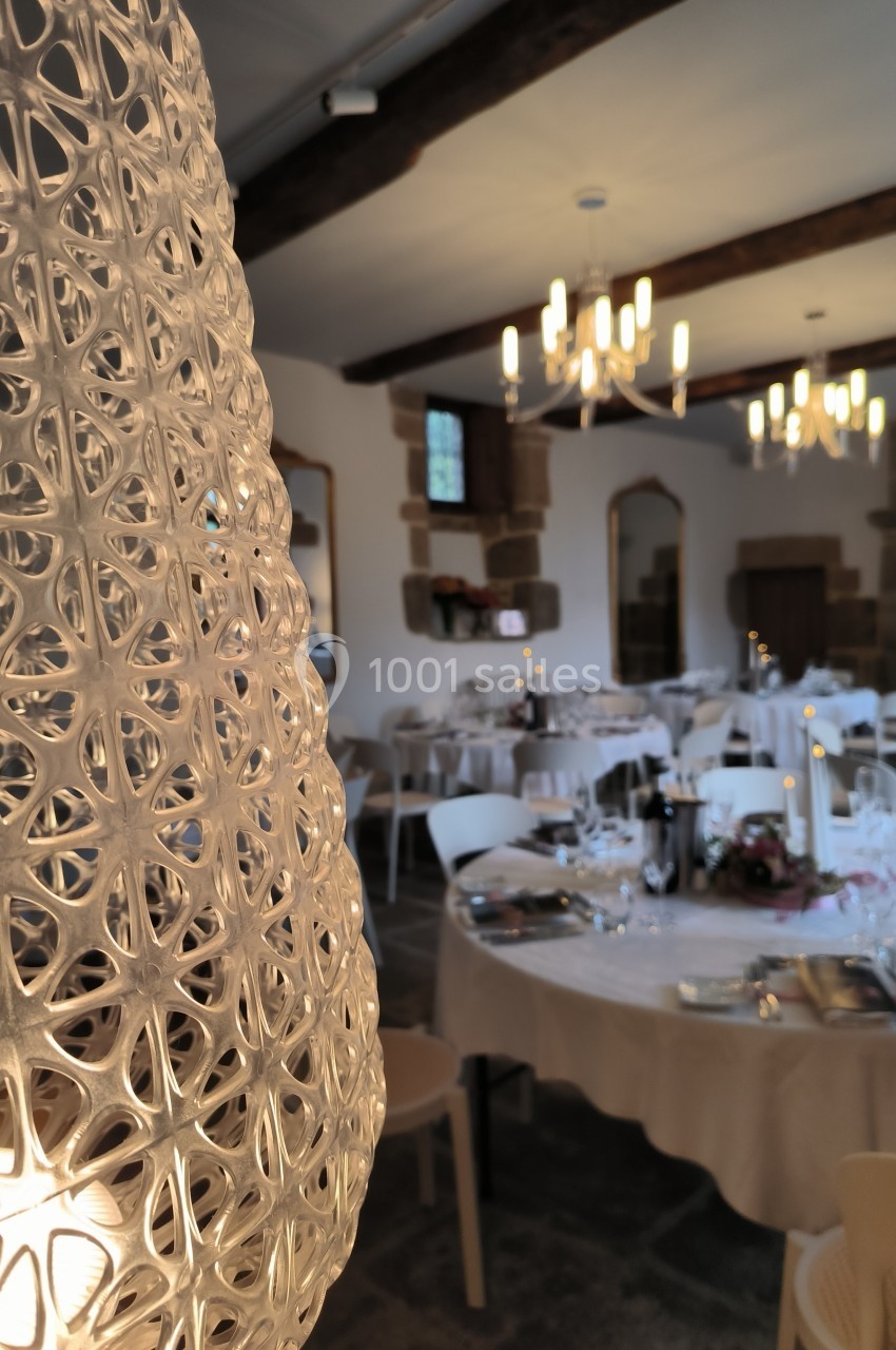 Salle de réception élégante avec tables dressées, lustres suspendus et un abat-jour ajouré au premier plan.