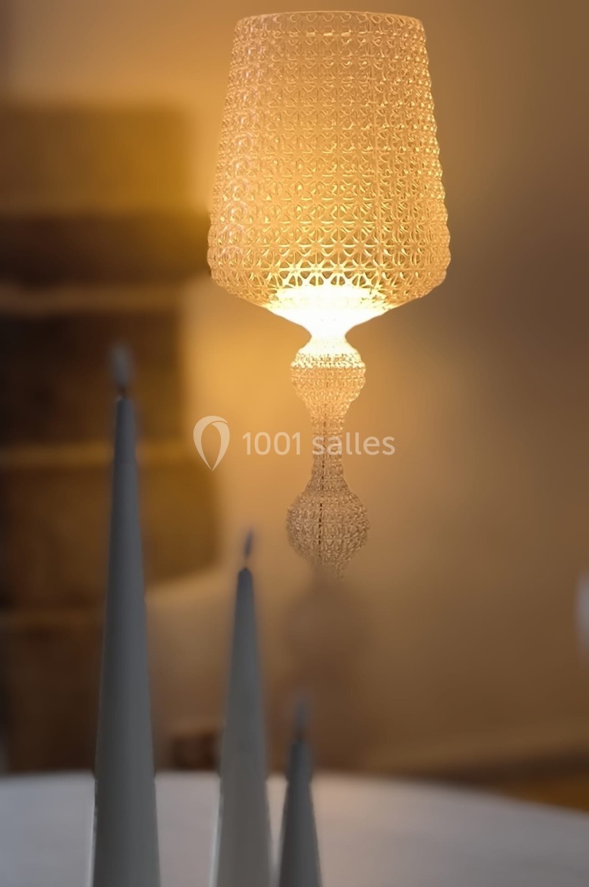 Lampe suspendue au design ajouré diffusant une lumière chaude, avec des objets coniques flous au premier plan.