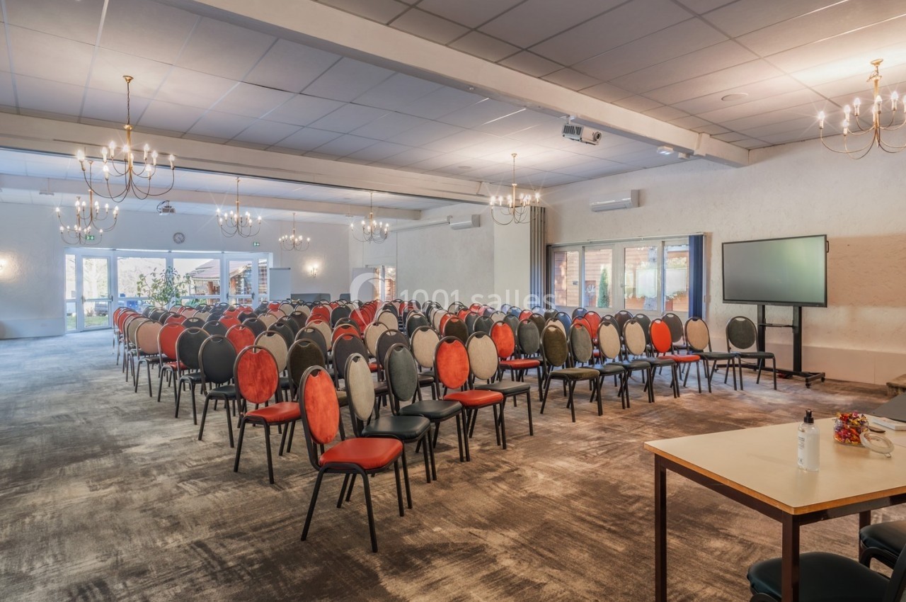 Salle de conférence lumineuse avec rangées de chaises colorées, écran de présentation et tables en arrière-plan.