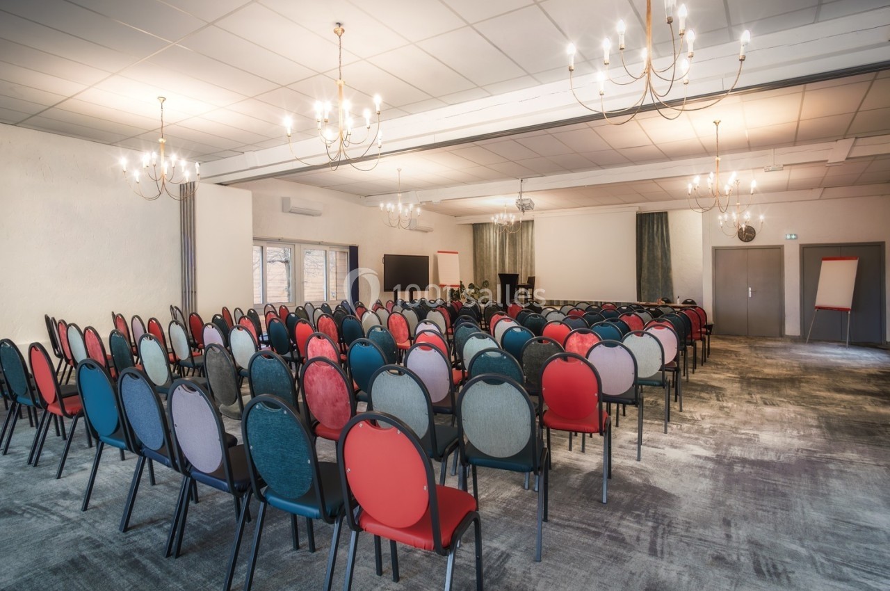 Salle de conférence lumineuse avec des rangées de chaises colorées, un écran, un pupitre et un chevalet.